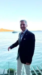 Michael Airo in a suit standing on a deck above the water, representing clarity, resilience, and strategic leadership.